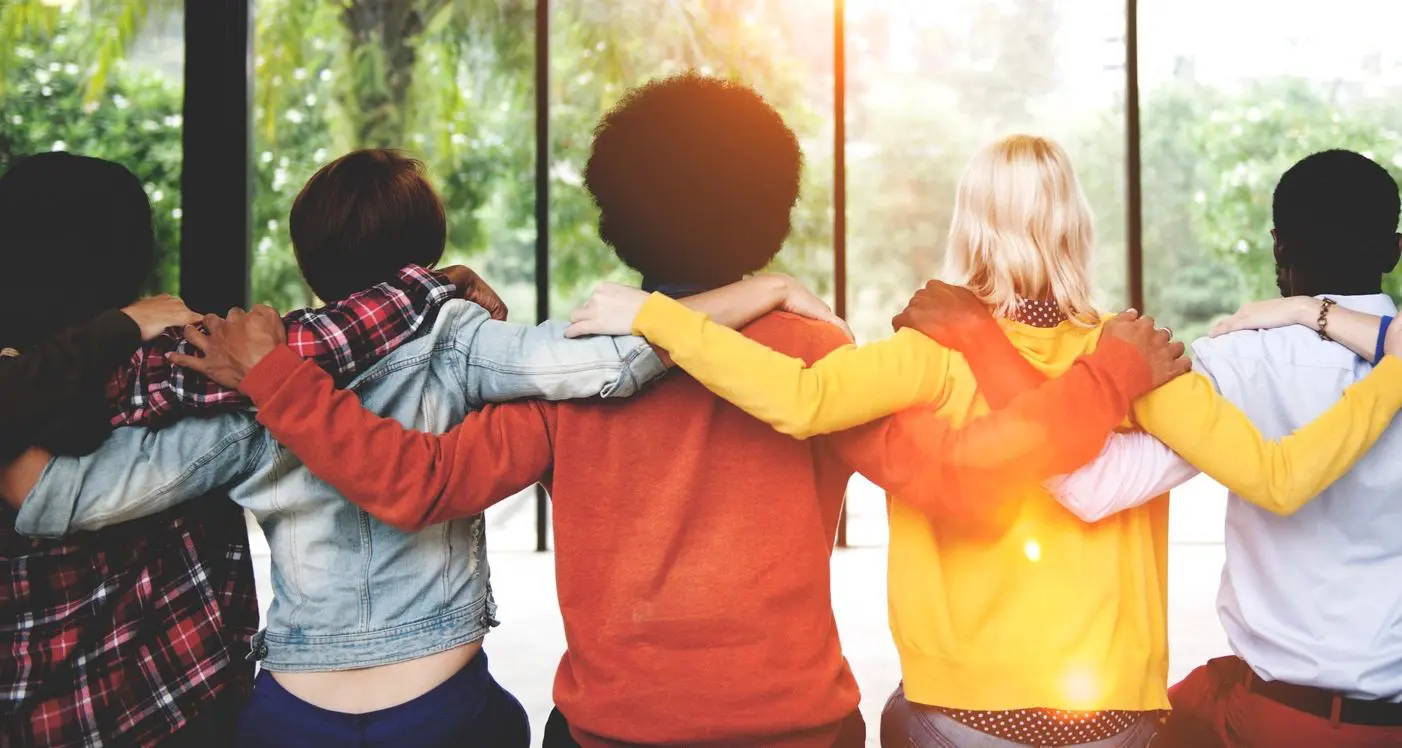 Three friends linking arms, facing a sunny window, sharing a moment of unity.