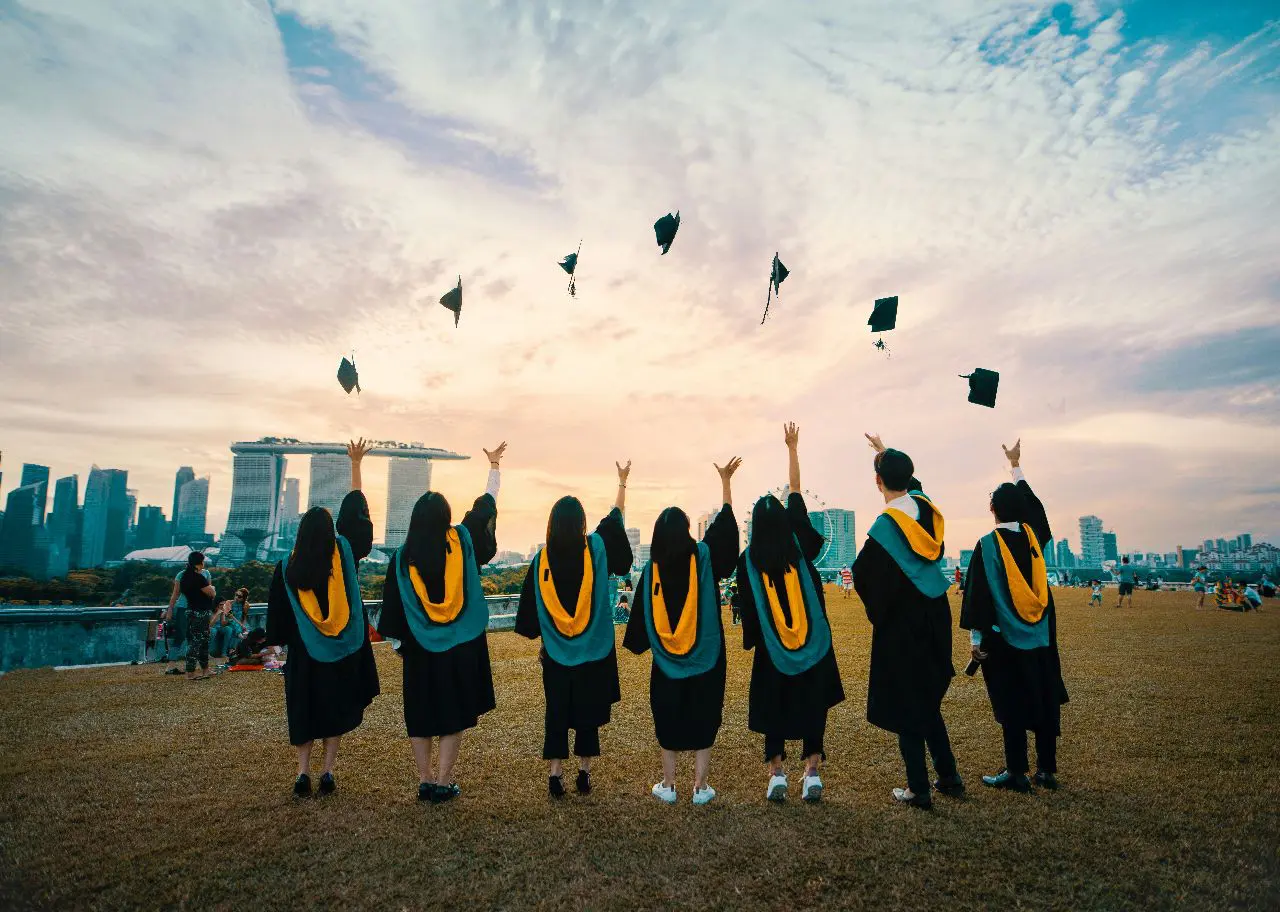 Graduates celebrate by tossing caps into the air at sunset.