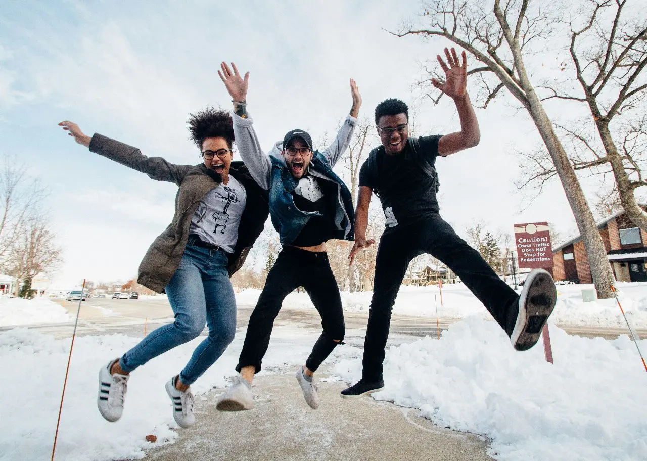 Three friends jumping joyfully outdoors in winter.