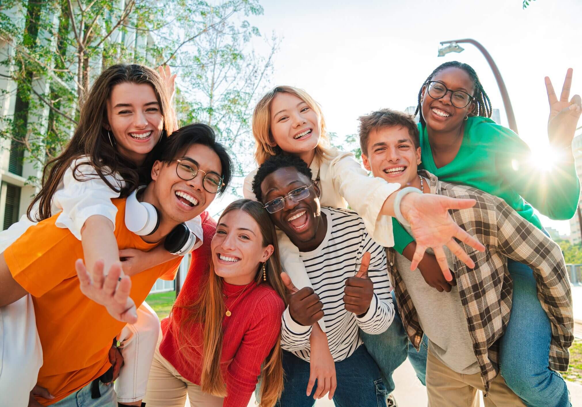 A diverse group of happy young friends reaching towards the camera outdoors.